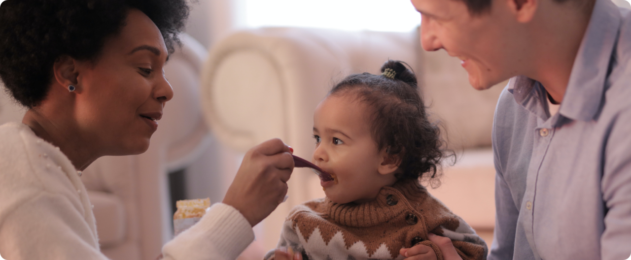 Two adults feeding a baby.
