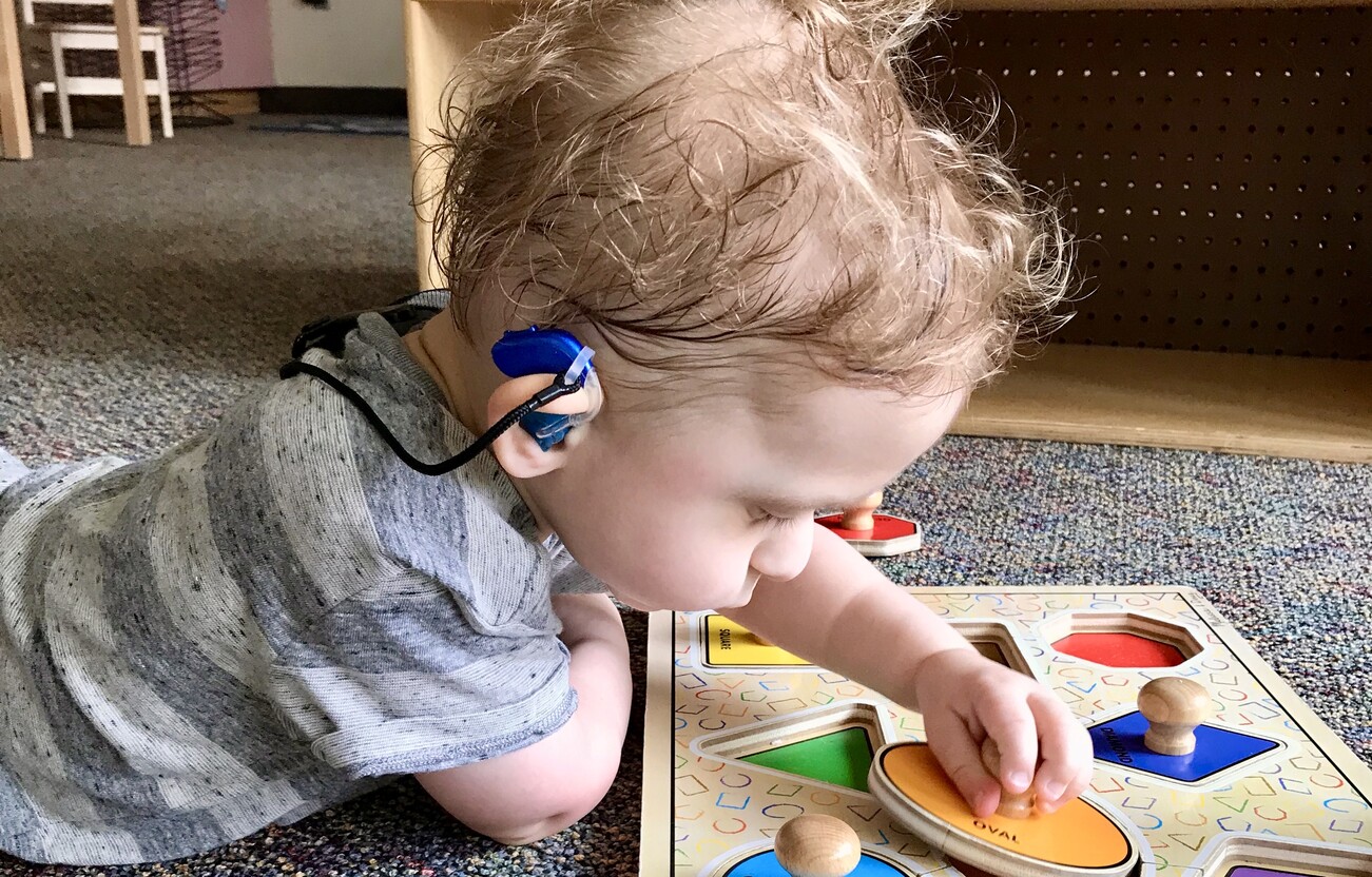 Child with hearing assistive technology playing with a puzzle