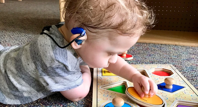 Child with hearing assistive technology playing with a puzzle