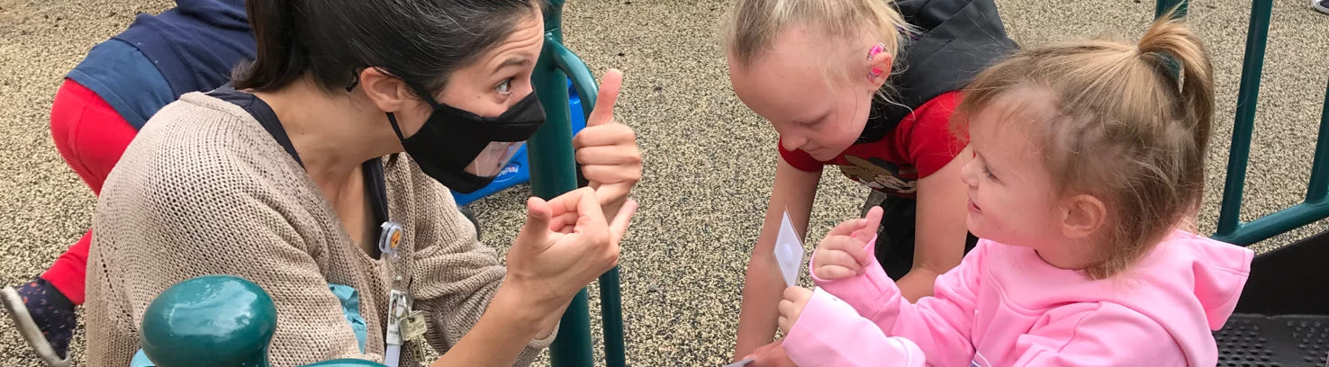 Teacher and a child signing to eachother on a playground