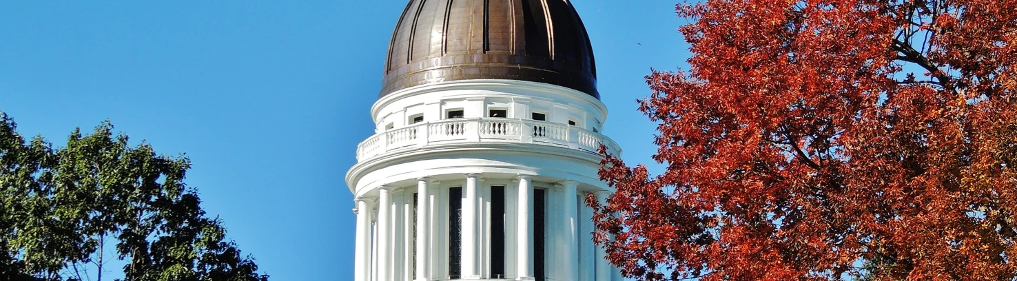Maine state capital building behind trees